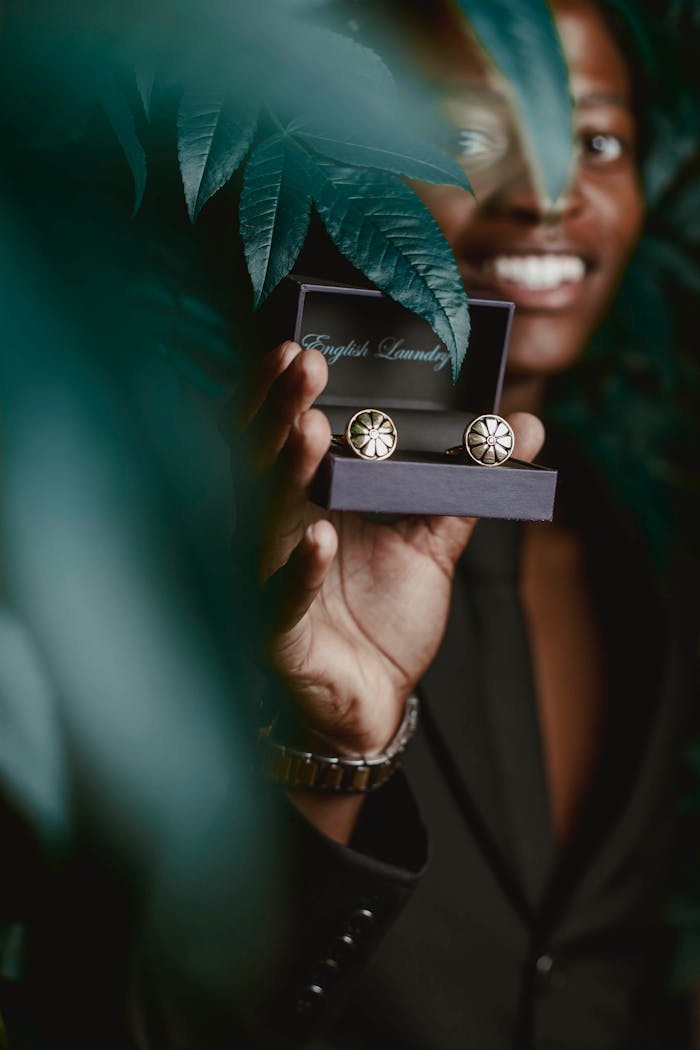 A person presents elegant cufflinks surrounded by lush green leaves, conveying luxury and style.